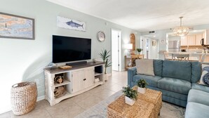 A modern living room with a flat-screen TV, a blue sofa, and a dining area with a chandelier. - Ocean Breeze 505 - NEW LISTING!! Gulf front, Updated Condo! (Perdido Key)