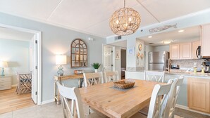 A spacious kitchen with modern appliances, a dining area with a wooden table, and a decorative ceiling light. - Ocean Breeze 505 - NEW LISTING!! Gulf front, Updated Condo! (Perdido Key)