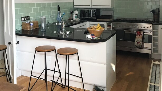 A modern kitchen with white cabinets, a black countertop, and a stainless steel range hood. There are two stools and a pair of shoes on the floor. - End terrace, sea views,short walk to the town and harbour of Ilfracombe (Ilfracombe)