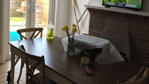 A dining area with a table, chairs, a television mounted on a brick wall, and a view through a glass door. - End terrace, sea views,short walk to the town and harbour of Ilfracombe (Ilfracombe)