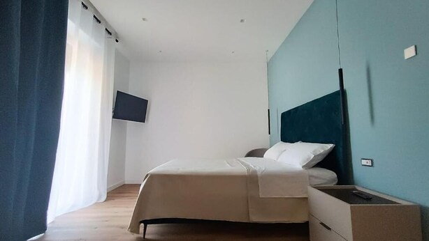 A bedroom with a bed, a TV mounted on the wall, and a wooden floor. - Le Chiavi di Polido (Aversa)