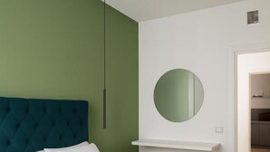 A modern bedroom with a large bed, a green accent wall, a round mirror, and a pendant light. - Le Chiavi di Polido (Aversa)