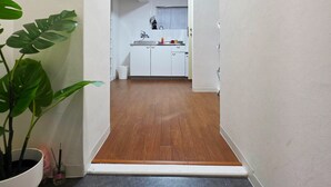 A narrow hallway leading to a kitchen with white cabinets, a sink, and a clock on the wall. - OLIVE stay (Fukuoka)