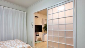 A hotel room with two beds, a sliding door, a TV, and a small desk with a chair. - OLIVE stay (Fukuoka)