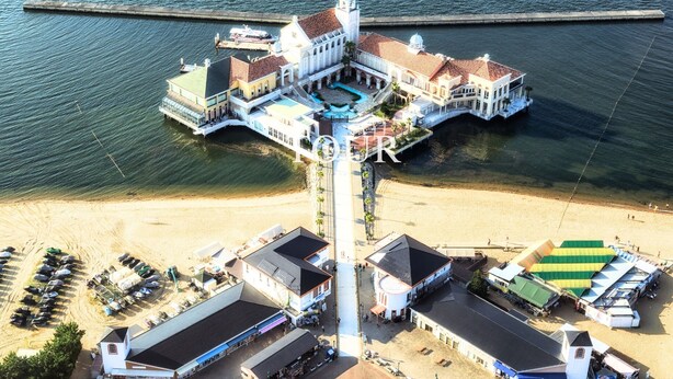 An aerial view of a coastal hotel with multiple buildings, a swimming pool, and a beach area. - OLIVE stay (Fukuoka)