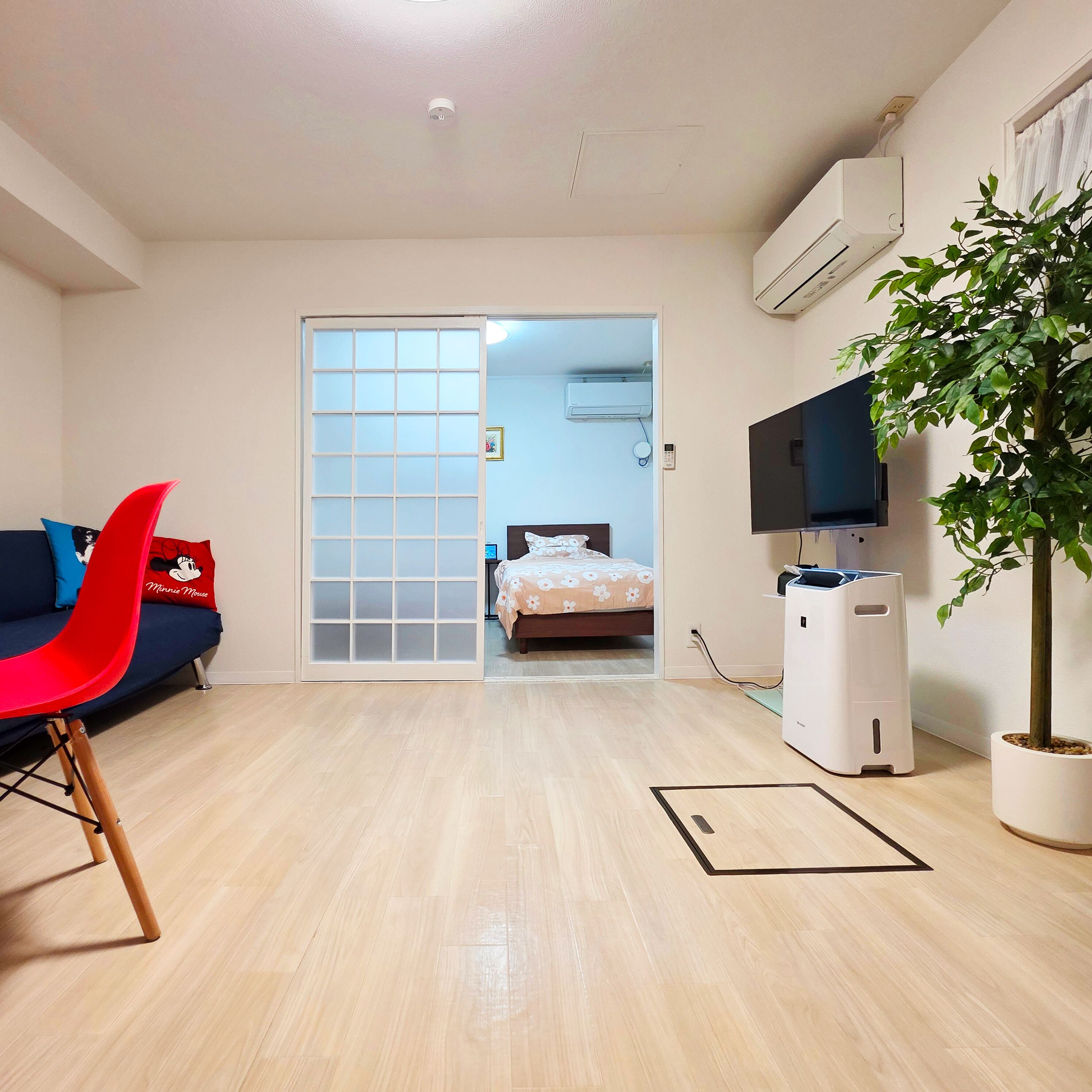 A room with a sliding door leading to a bedroom, a TV, a plant, and a red chair.
