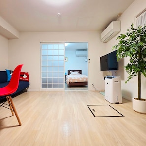 A room with a sliding door leading to a bedroom, a TV, a plant, and a red chair. - OLIVE stay (Fukuoka)