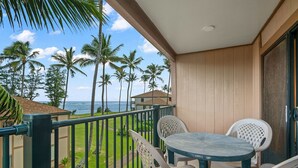 Un balcon avec vue sur l’océan et les palmiers, comprenant une table et deux chaises.