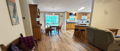 A spacious living area with a wooden floor, a dining table with chairs, a sofa, and a kitchen in the background.