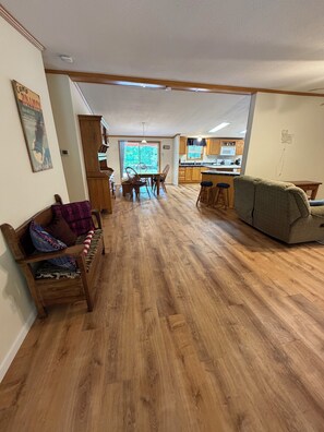 Een ruime woonkamer met houten vloer, een eettafel met stoelen, een bank en een keuken op de achtergrond.