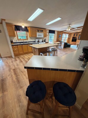 A kitchen with wooden cabinets, a central island, bar stools, a microwave, and a stove.