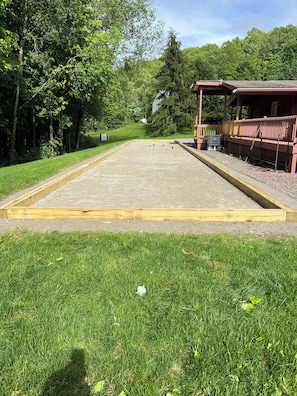 A courtyard with a lawn, a wooden deck, and a building with a covered seating area. - Cozy, PRIVATE, 4-bedroom cabin on 40 acres. (Markleton)