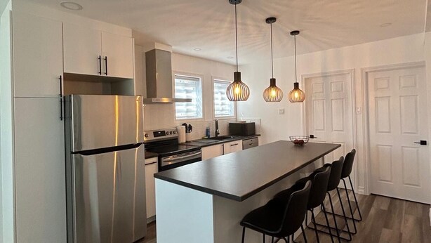 Una cocina moderna con una isla central, electrodomésticos de acero inoxidable, iluminación colgante y una zona de bar con taburetes.