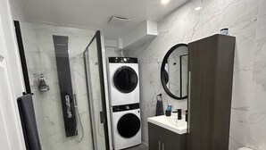 Un baño moderno con cabina de ducha de vidrio, lavadora integrada, armario de madera oscura y un inodoro.