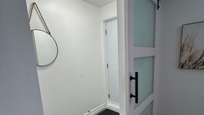 Un pasillo con una puerta corredera, una alfombra blanco y negro, un accesorio de iluminación y una obra de arte enmarcada en la pared.