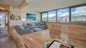 Una sala de estar moderna con un ventanal grande, un conjunto de sofás, una mesa de comedor y vistas a un paisaje urbano.