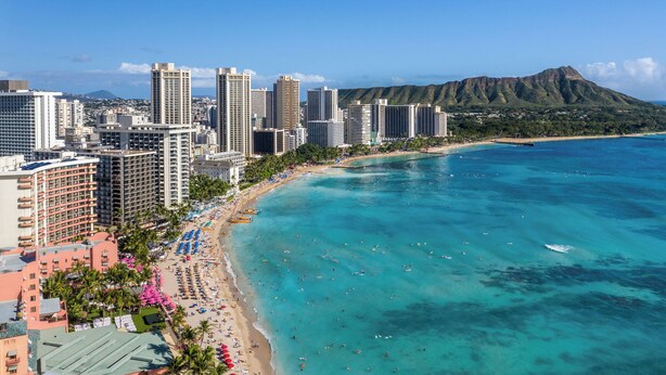 Un paisaje urbano costero con rascacielos, una playa y una montaña al fondo.