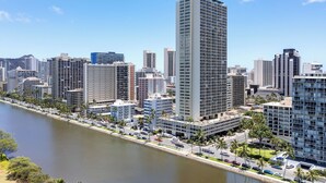Un edificio alto con un marcador rojo que indica la ubicación, rodeado de otros edificios modernos, un río y palmeras.
