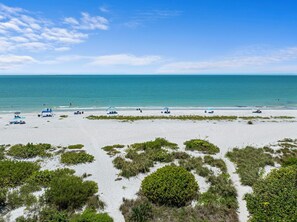 A beach with clear skies, calm waters, and sparse vegetation. - Wake beachfront and enjoy effortless beach days at Loggerhead Cay 264! This top-floor 2BR/2BA Sanibel condo includes 2 bikes, beach gear, a heated pool, tennis, pickleball and everything you need for an easy island vacation—just steps from the beach (Sanibel Island)