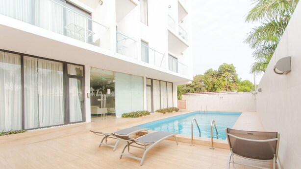 Un bâtiment moderne doté d’une piscine, de portes vitrées et d’un patio aménagé avec des chaises longues.