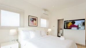 Une chambre d’hôtel avec un grand lit, deux tables de chevet, une télévision et une fenêtre avec des stores.