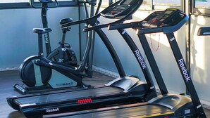 Ein Laufband und ein Crosstrainer in einem Raum mit großen Fenstern.