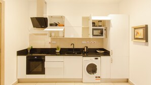 Eine kompakte Küche mit einbauendem Backofen, Mikrowelle und Waschmaschine, mit weißen Schränken und einer schwarzen Arbeitsplatte.