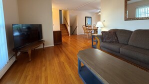 Ein Wohnzimmer mit Fernseher, Sofa und Holzboden.