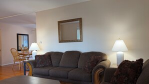 Ein Wohnzimmer mit einer Couch, zwei Sesseln, einem Couchtisch, einem Esstisch und zwei Lampen.