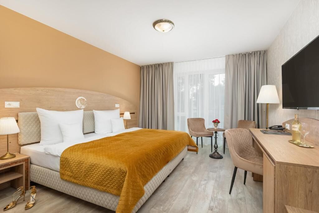 A hotel room with a bed, a desk, a chair, a TV, and a window with curtains.