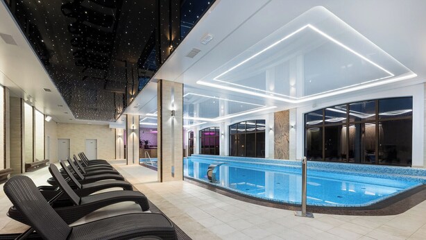 Un'area piscina interna moderna con acqua cristallina, lettini prendisole e un design del soffitto contemporaneo.