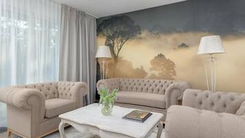 A living room with a beige sofa set, a coffee table with a vase and book, and a large painting on the wall.