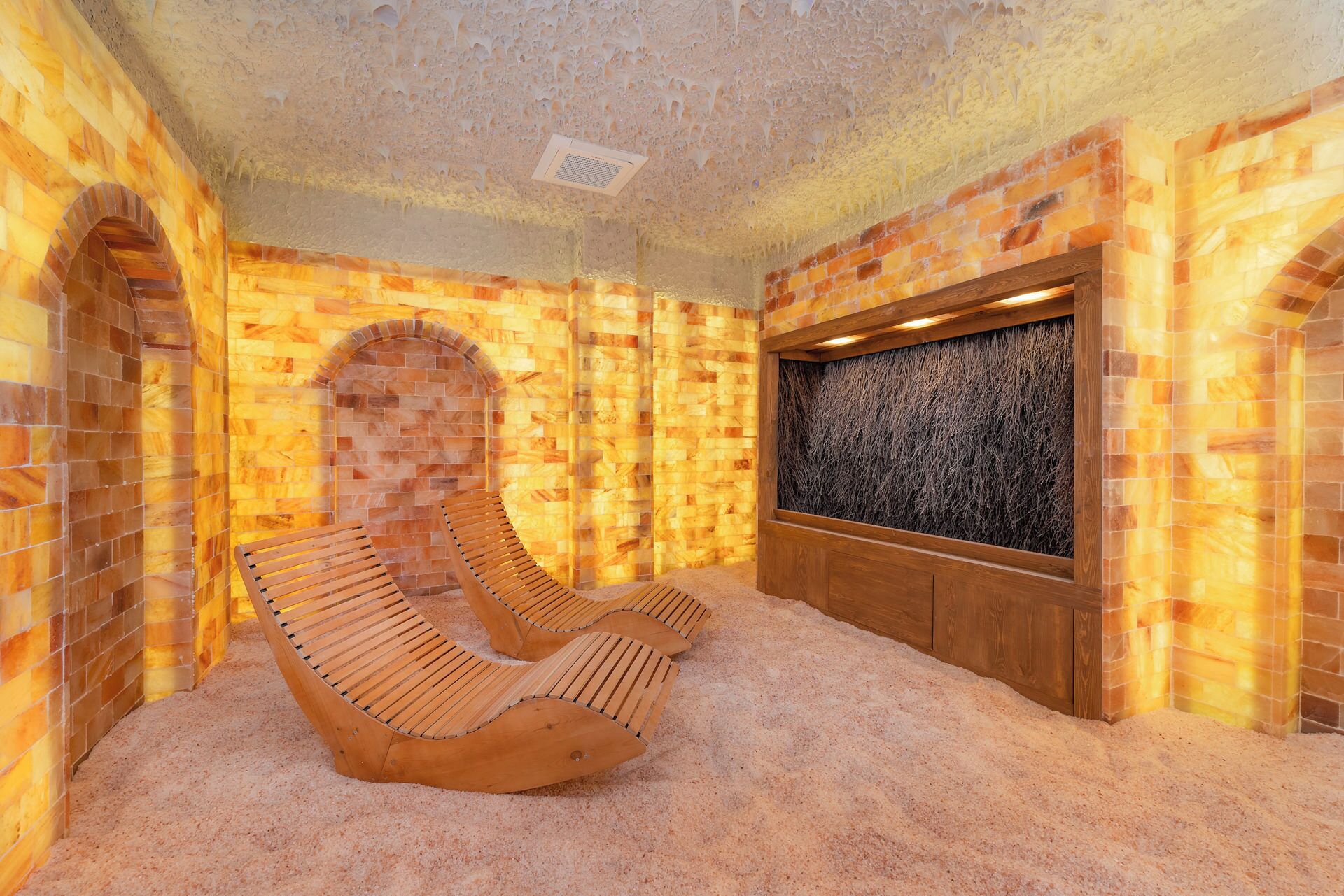 Un sauna con bancos de madera, pared de piedra y panel de madera con diseño texturizado.