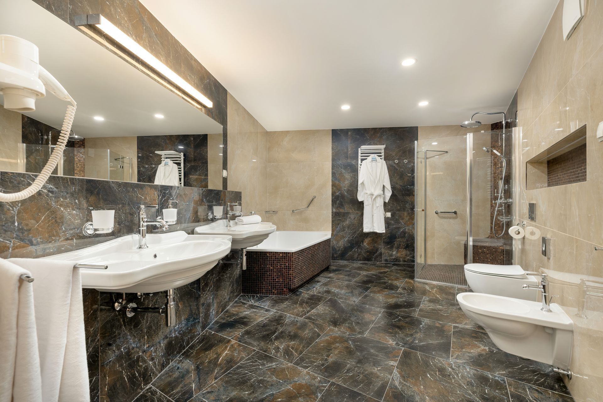 A modern bathroom with three sinks, a bathtub, a shower, and a toilet.