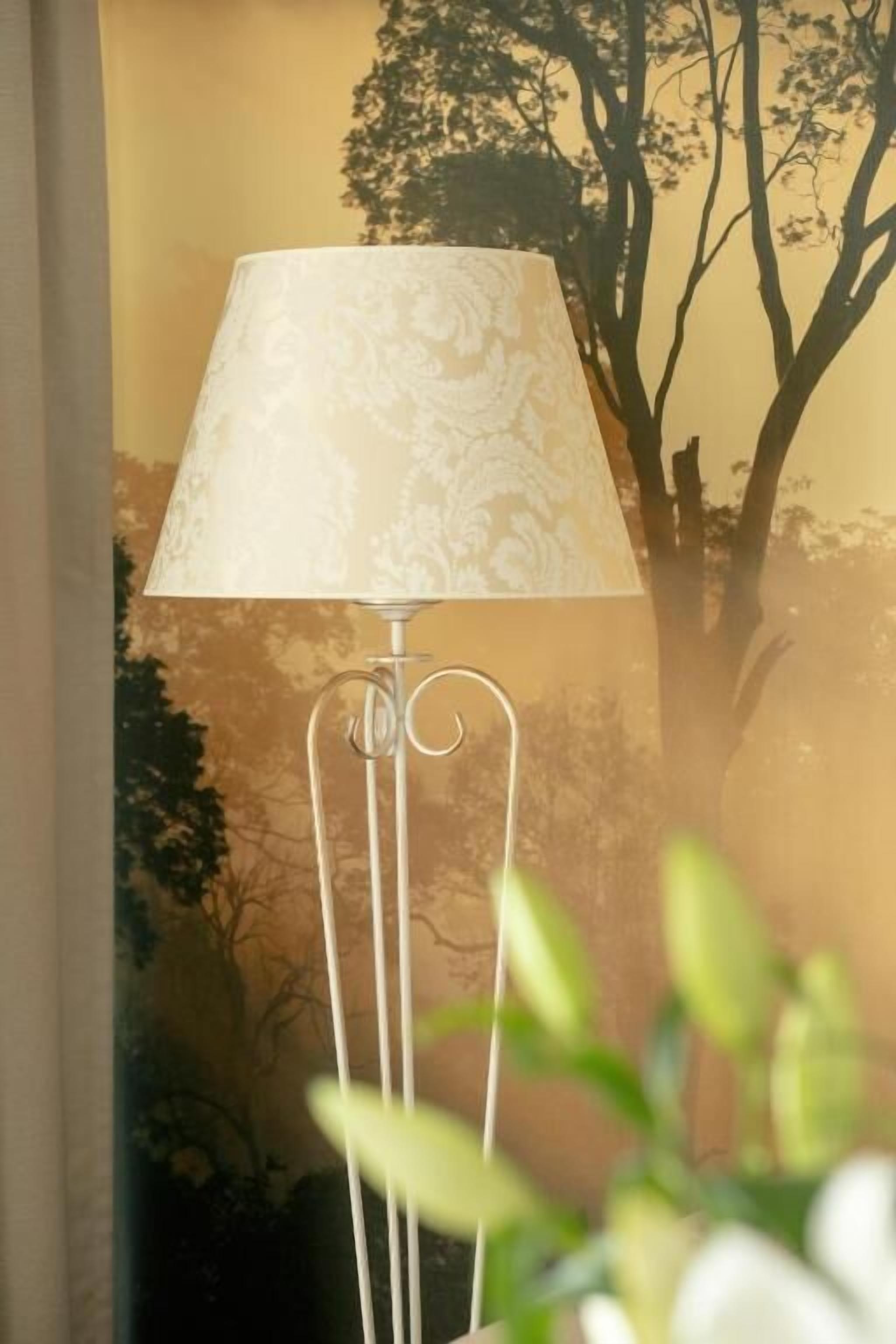 A floor lamp with a patterned lampshade in a room with a mural of trees on the wall.