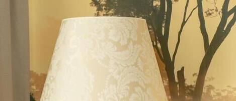 A floor lamp with a patterned lampshade in a room with a mural of trees on the wall.