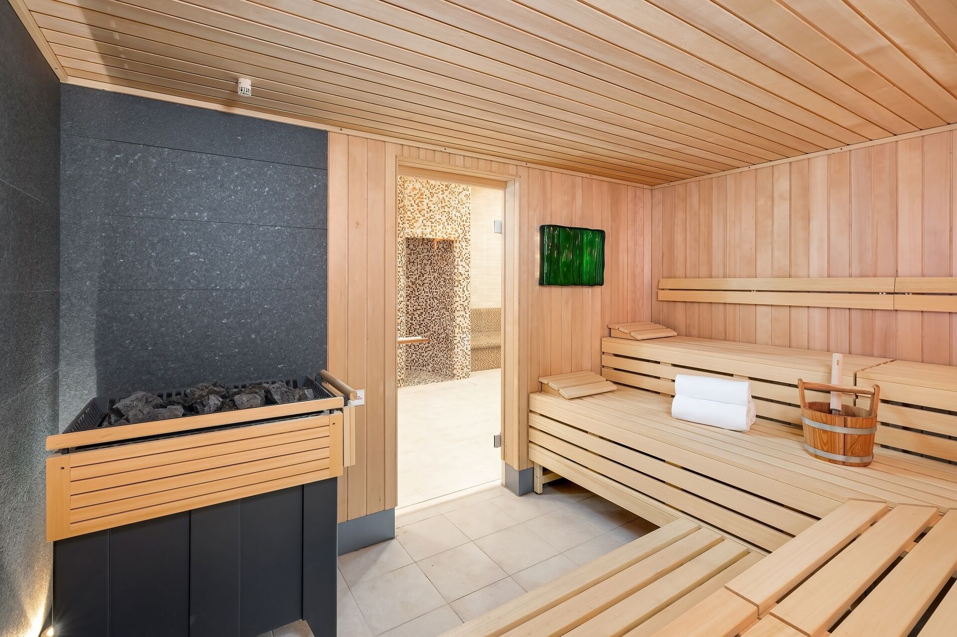 A sauna room with wooden benches, a stone wall, and a sauna heater.