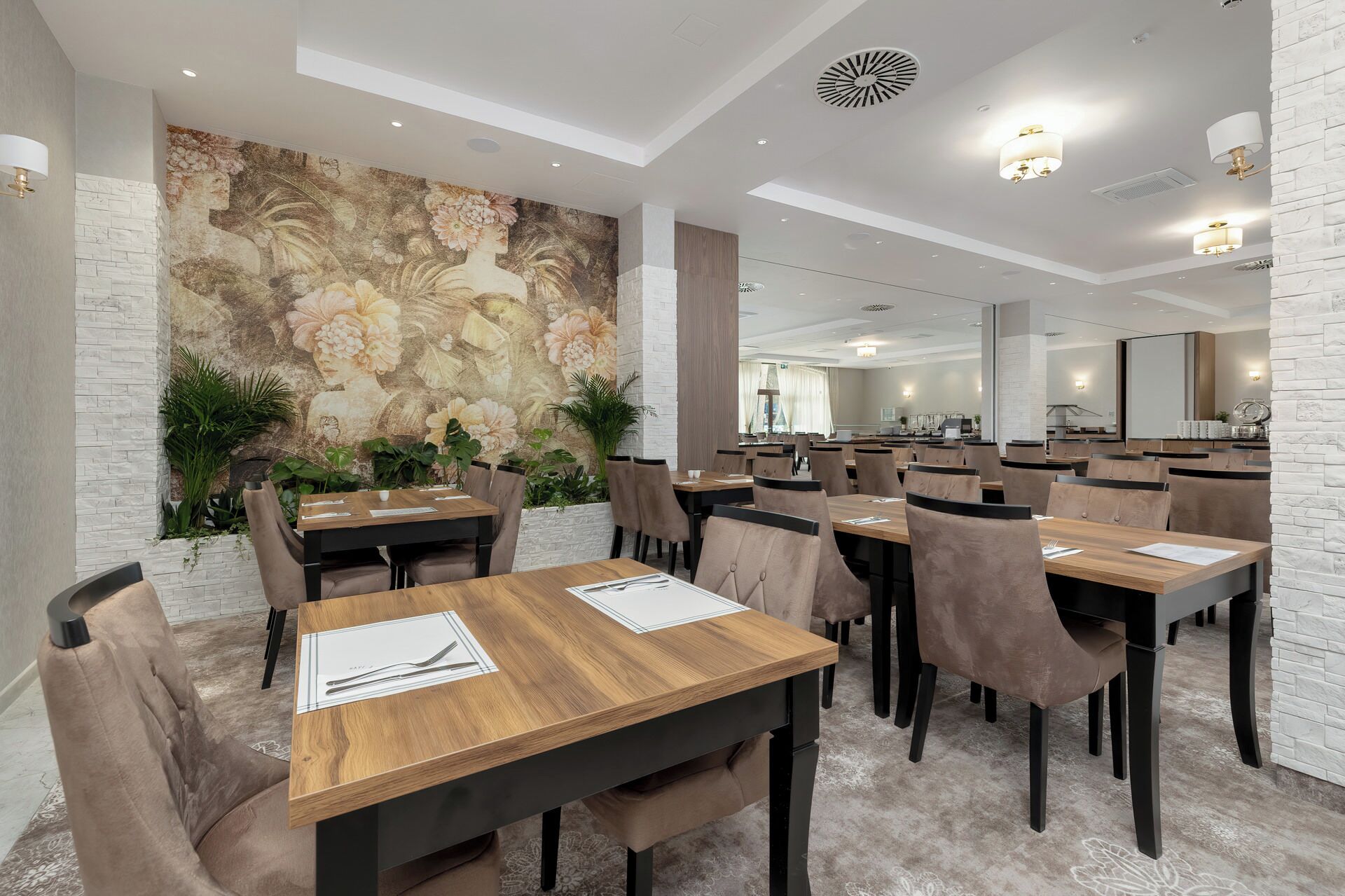 A modern dining area with wooden tables and chairs, a decorative mural on the wall, and a large mirror reflecting the space.
