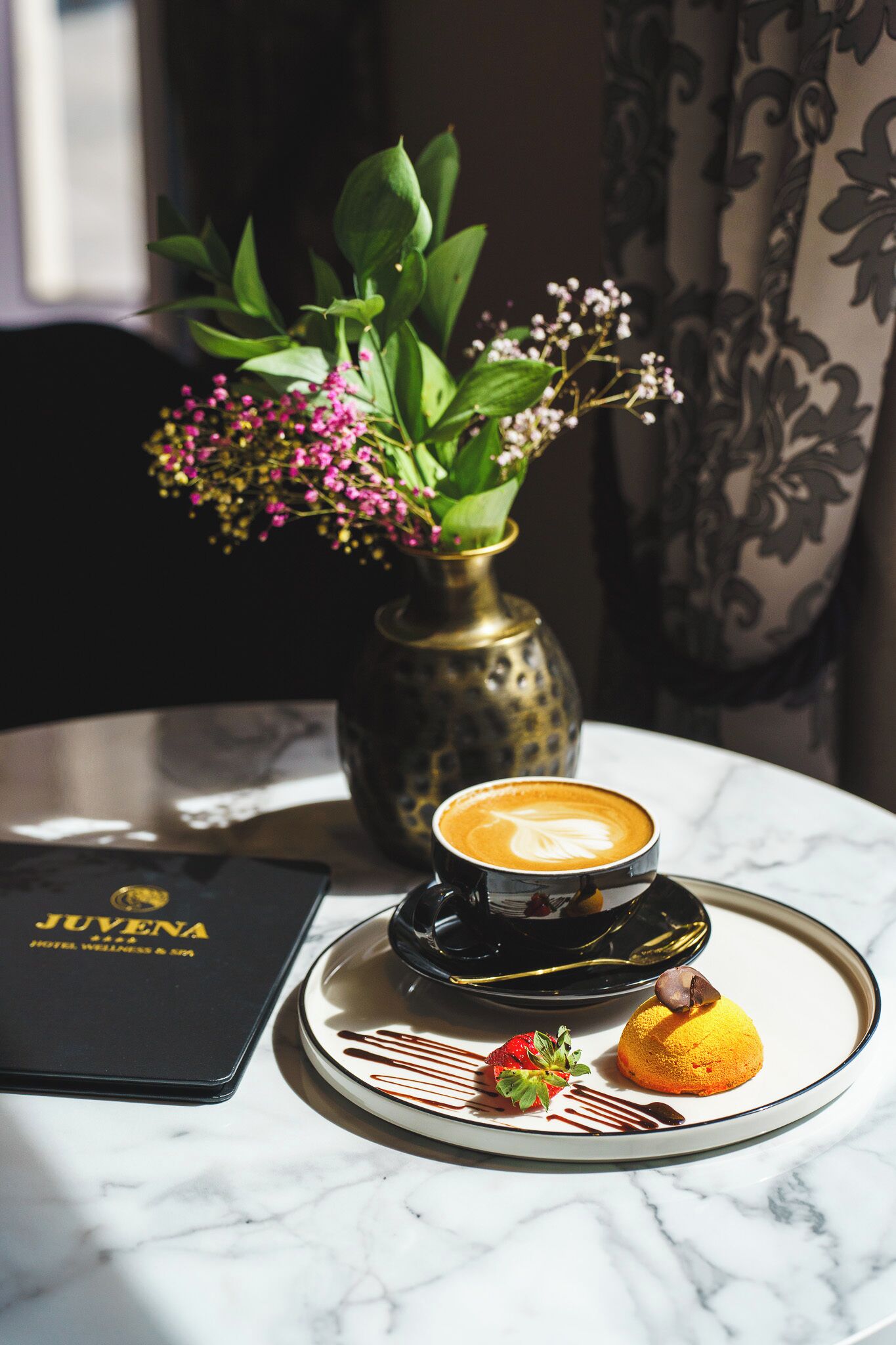 En desserttallerken med en kaffedrik, et stykke chokolade og en jordbær på et marmorbord.