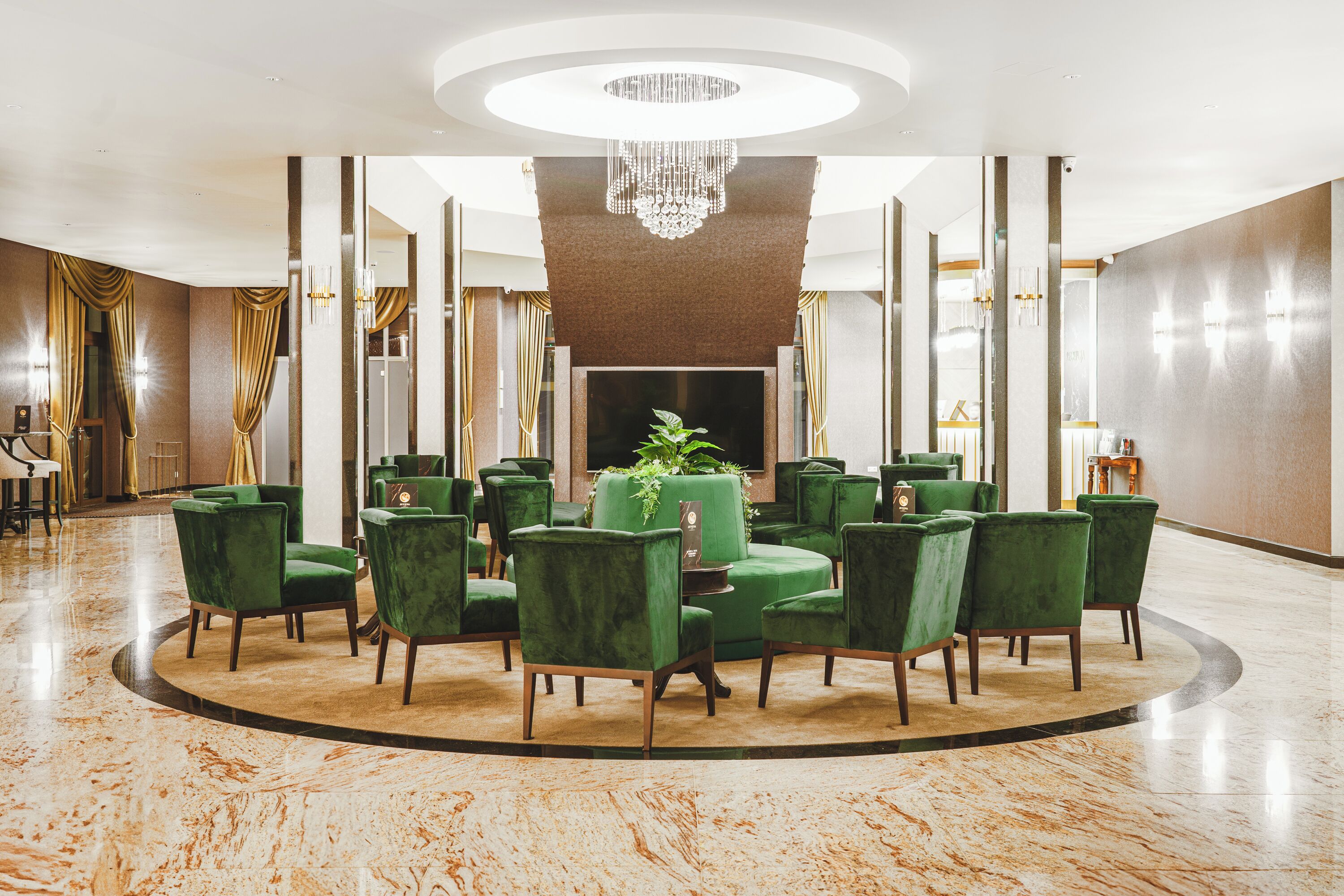 A lobby with a circular seating arrangement, a chandelier, and a large plant.