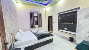 Quarto com cama, televisão na parede, aparelho de ar condicionado e janela com cortinas.