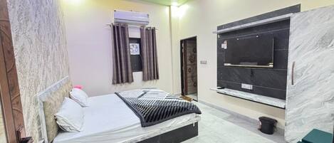 A bedroom with a bed, a TV mounted on the wall, an air conditioning unit, and a window with curtains.