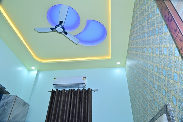 A ceiling fan with a blue light, an air conditioning unit, and a patterned wall. - GOLDEN VENTURE HOTES PRIVATE LIMITED (Khatoo)