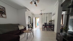 Ein Wohnzimmer mit einer Couch, einem Esstisch mit Stühlen, einem Fernsehtisch und einer Küchenzeile.