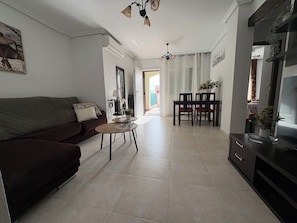 A living room with a sofa, a dining table with chairs, a TV stand, and a kitchen area. - Apartment on Avenue de la Mancha, across from the pool and a 15-minute walk to the beach (Torrevieja)