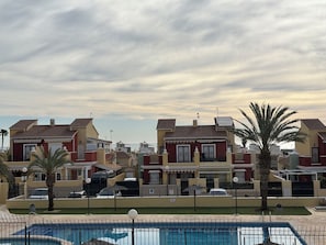 A residential area with a swimming pool, houses with red and yellow facades, and a palm tree. - Apartment on Avenue de la Mancha, across from the pool and a 15-minute walk to the beach (Torrevieja)
