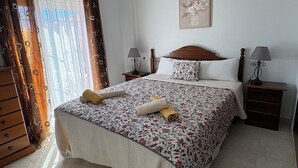 Ein Schlafzimmer mit einem großen Bett, zwei Nachttischen mit Lampen, einer hölzernen Kommode und einem Fenster mit Vorhängen.