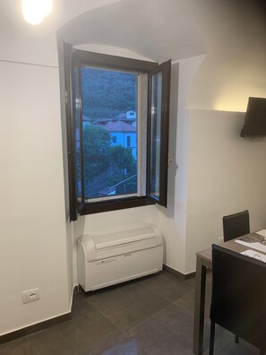 A room with a corner window, a white radiator, a dining table with chairs, and a wall-mounted TV. - Vacation home "A Cola" hot tub and natural ponds of Rio Barbaira (Rocchetta Nervina)