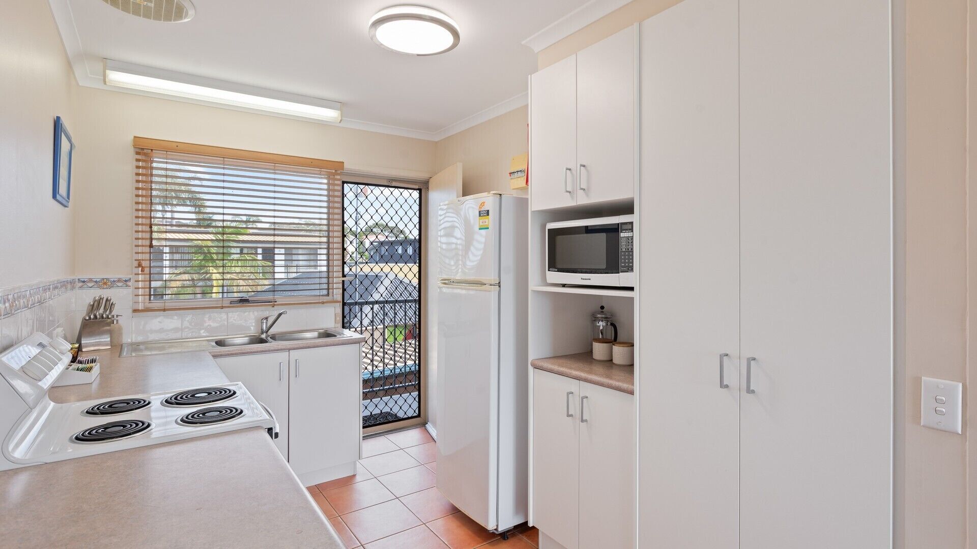 A compact kitchen with white cabinets, a stove, a microwave, and a sink.