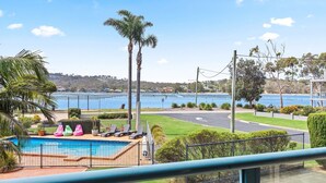 A pool area with lounge chairs and a view of a lake and distant buildings. - Fishpen Views - Merimbula (Merimbula)